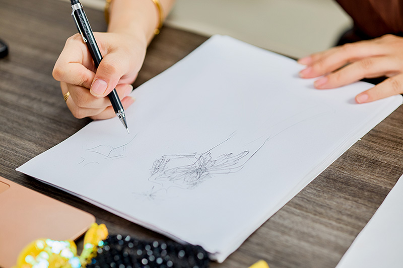 Bozzetto couture disegnato a mano da un designer su una scrivania, accanto a materiali per perline