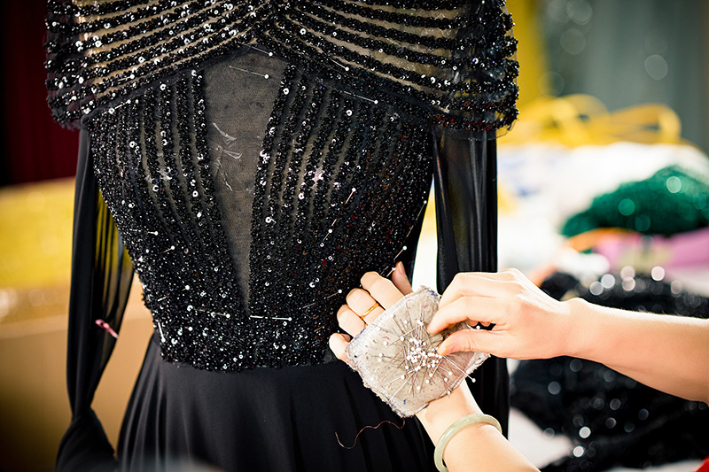 Un'operatrice fissa con spilli una decorazione di paillettes sul corpetto di un abito nero